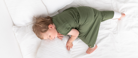 Un bambino che dorme pacificamente su un letto bianco, indossando un sacco nanna verde, abbracciando un cuscino e rilassato nel sonno.