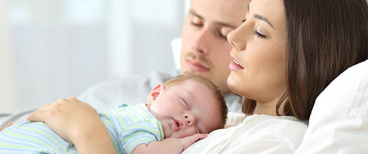 Una coppia riposa con il loro neonato addormentato sul petto della madre, creando un'immagine di intimità e tranquillità familiare, simbolo di amore e protezione.