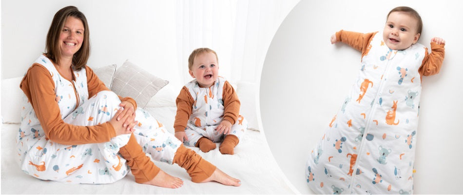 Una madre e il suo bambino indossano sacchi nanna coordinati con fantasia di animali, sorridendo e seduti su un letto, mostrando comfort e calore.