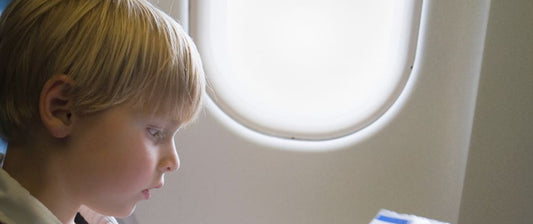  Un bambino dai capelli biondi è seduto accanto al finestrino di un aereo, guardando attentamente qualcosa tra le sue mani, concentrato durante il volo.
